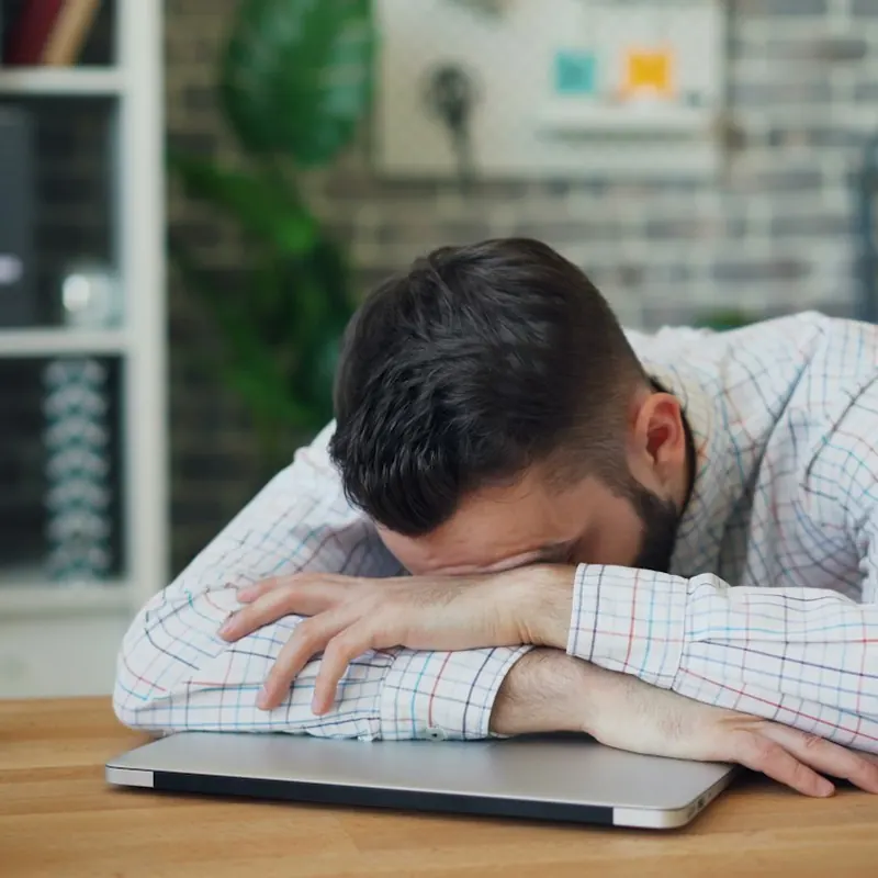 Homem exausto com a cabeça sobre o notebook