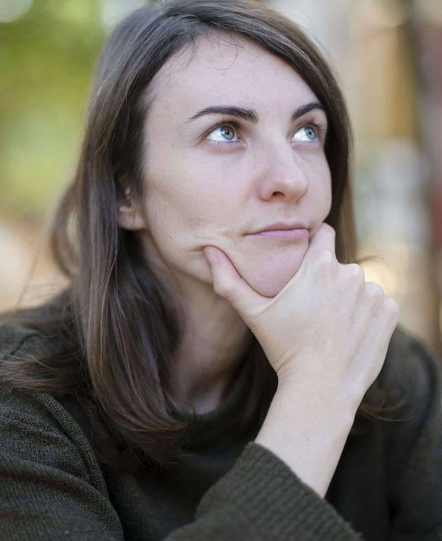 Mulher pensativa com a mão no queixo: a procrastinação é uma resposta emocional, não preguiça